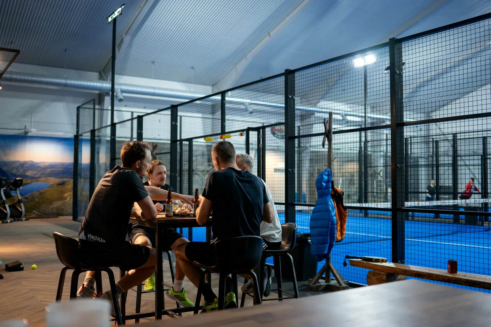 Ett gäng sitter vid ett bord intill padelbanorna och pratar efter spelet.