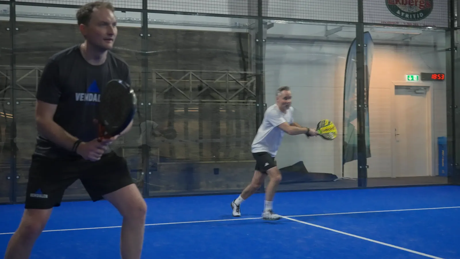 En spelare står redo vid nätet medan motspelaren slår en boll.